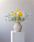 Sunny Days: yellow, white and sky-blue poppies in a weathered stone vase on a white plinth