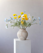 Sunny Days: yellow, white and sky-blue poppies in a weathered stone vase on a white plinth